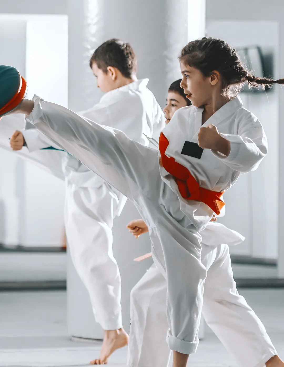 A girl in a Taekwondo uniform mid-kick, eyes on the target