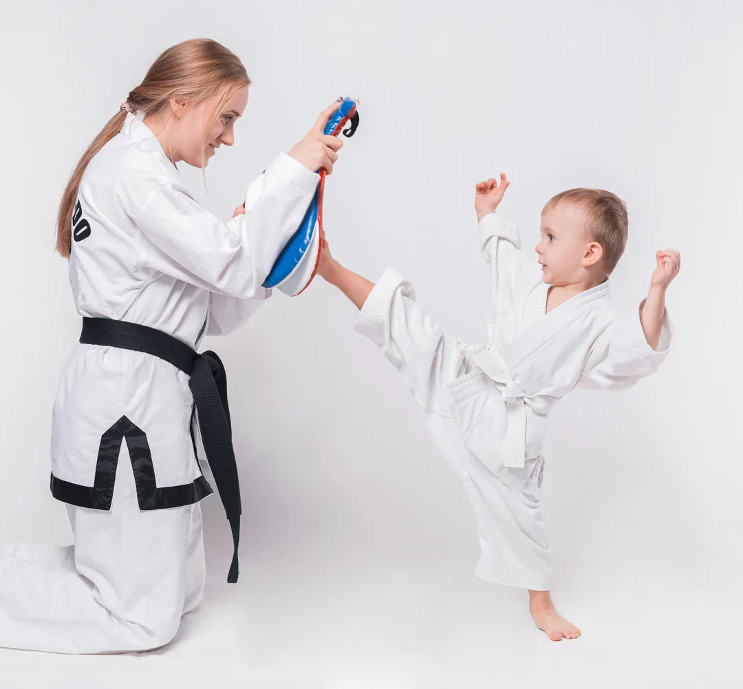 A young child in a Taekwondo uniform throws a punch, sunlight on her face